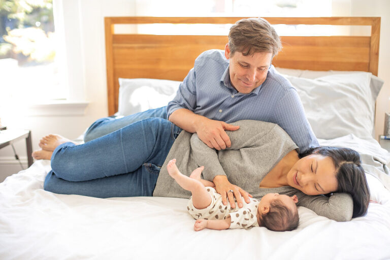 mother and father relax on bed with  newborn baby  in san jose at home