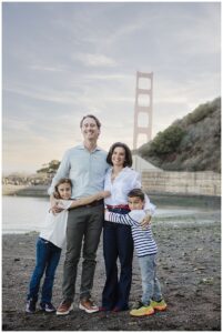 family posing on rocky beach at Fort Baker with Golden Gate Bridge visible behind them"