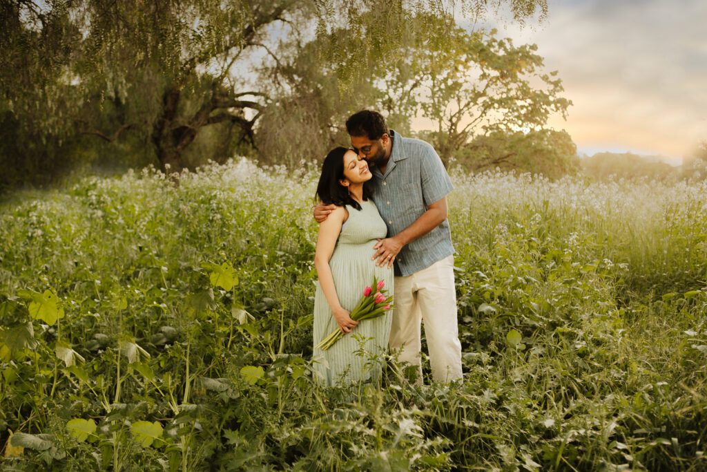 couple kissing in wildflower fields during maternity photo shoot
