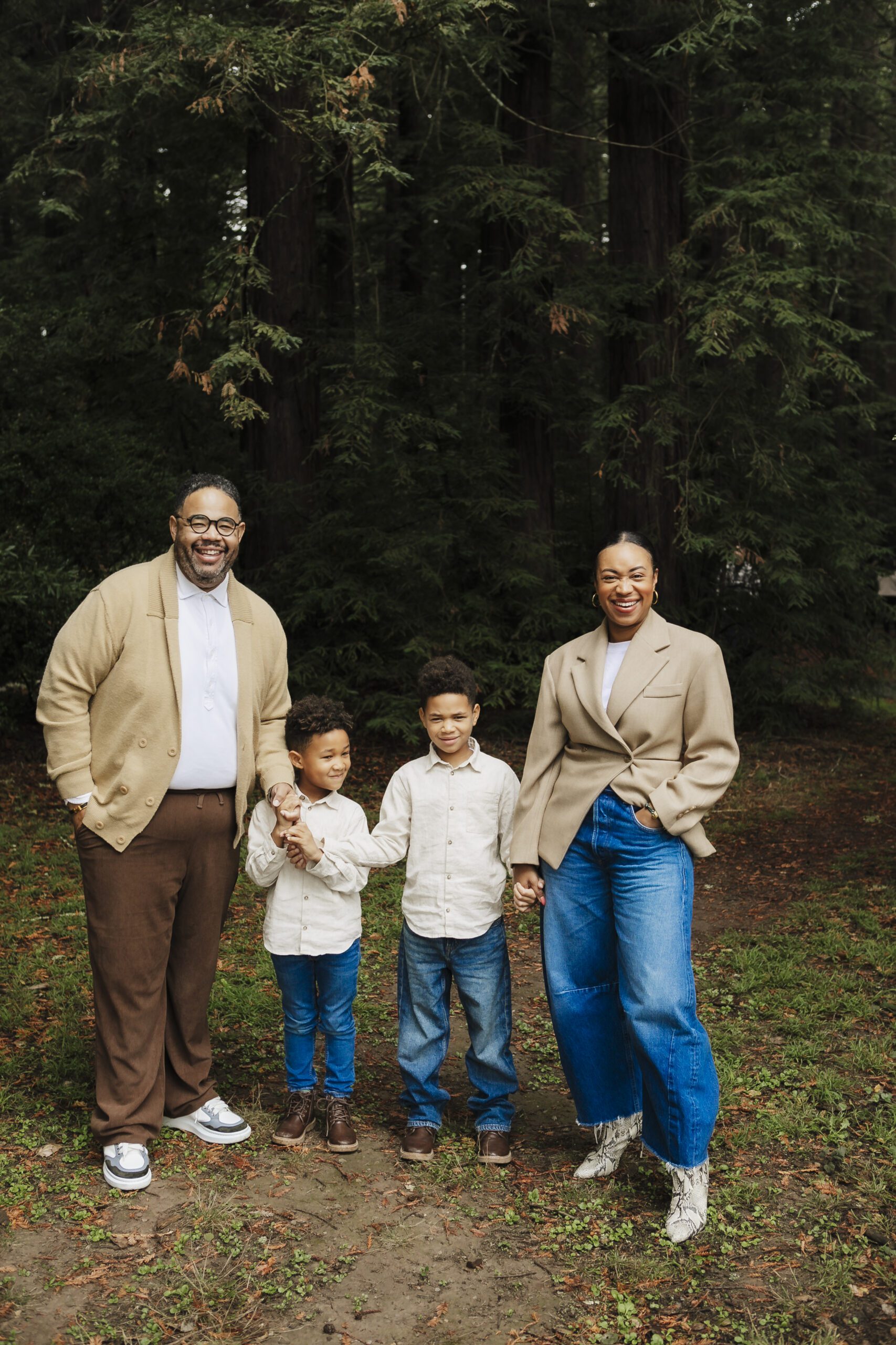 St. Louis family photographer, parents and their two young sons holding hands together under tall trees