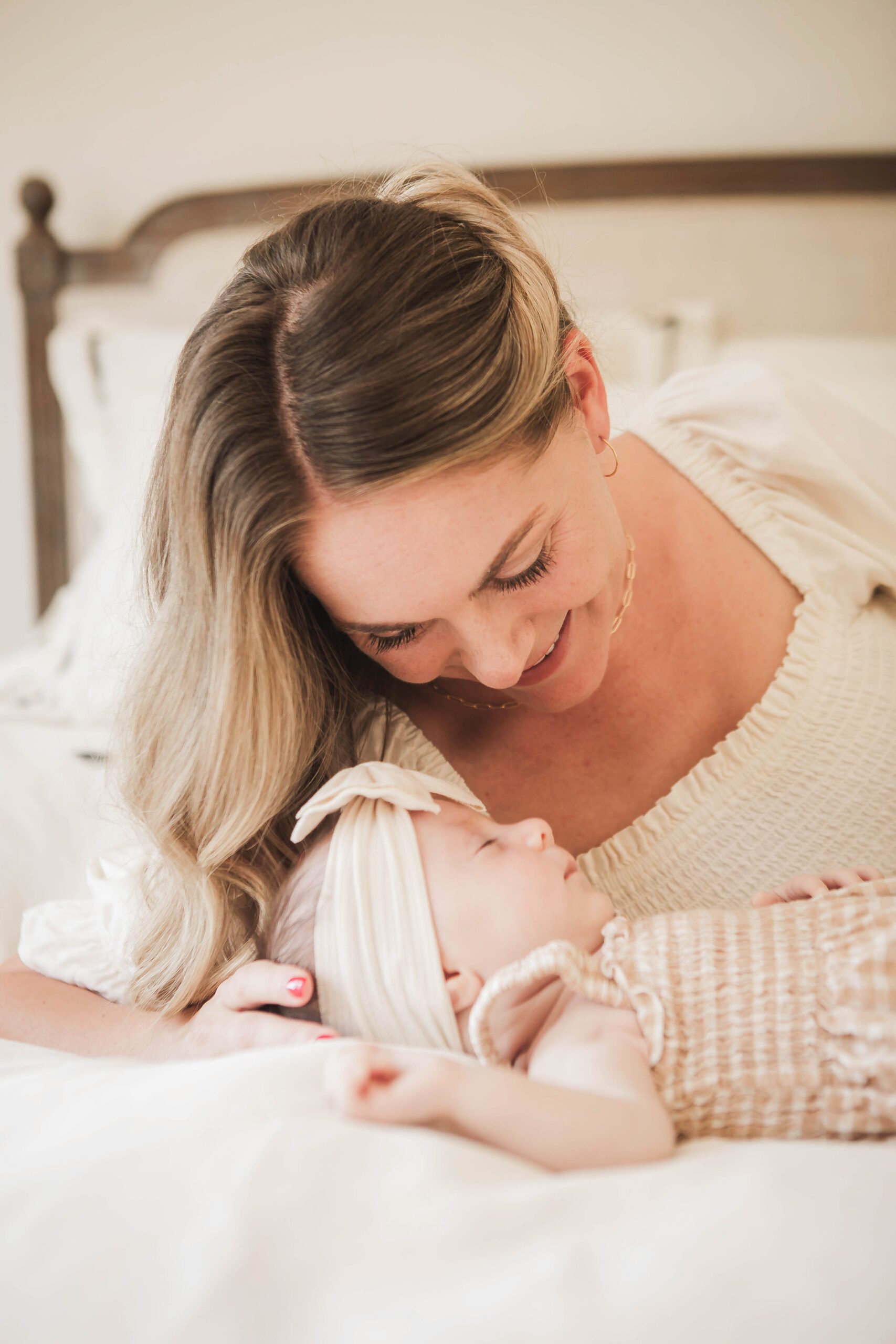 St. Louis newborn photographer, mother in a cream dress smiling down at her newborn daughter in a bow headband