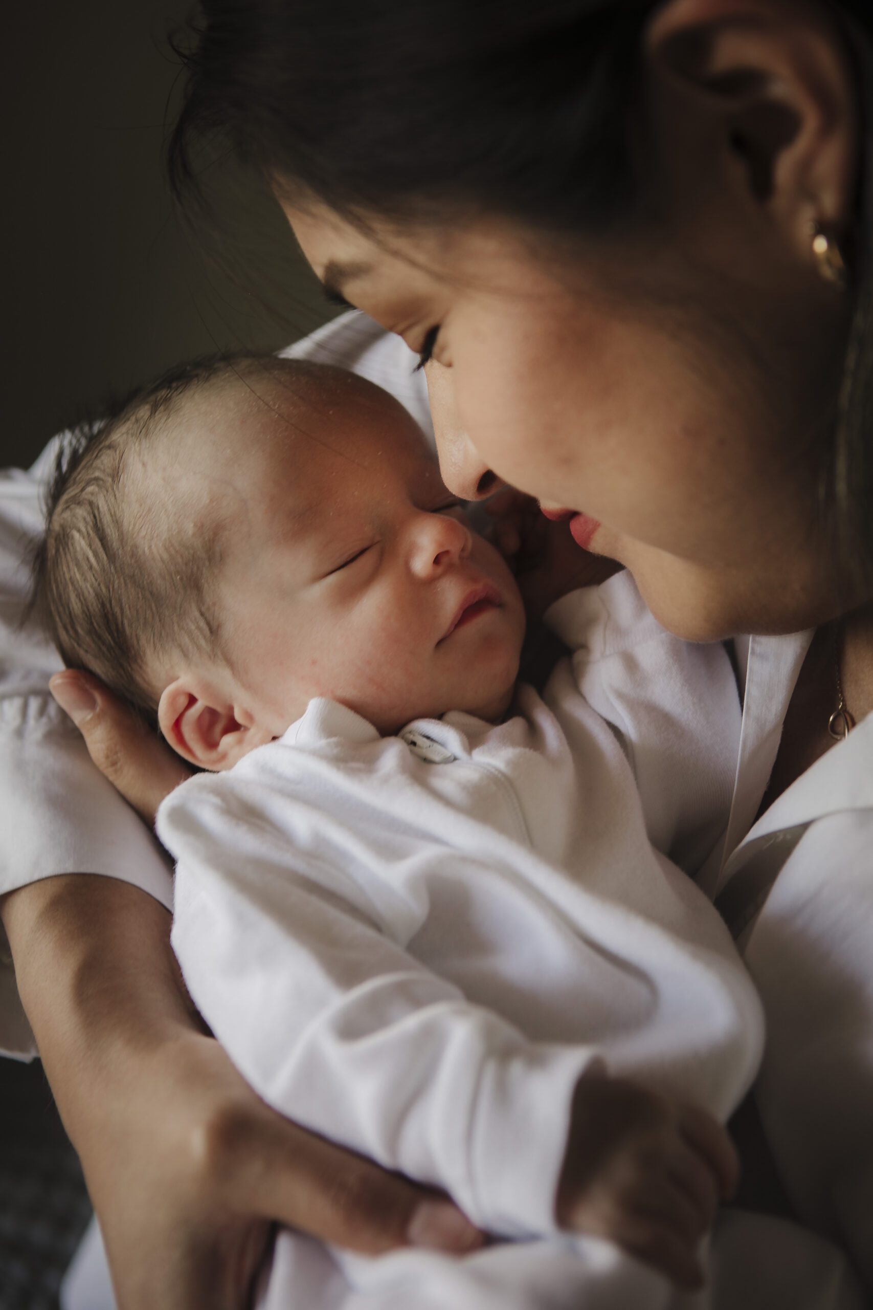 St. Louis newborn photographer, mother gently touching noses with her sleeping newborn dressed in white in a tender close up