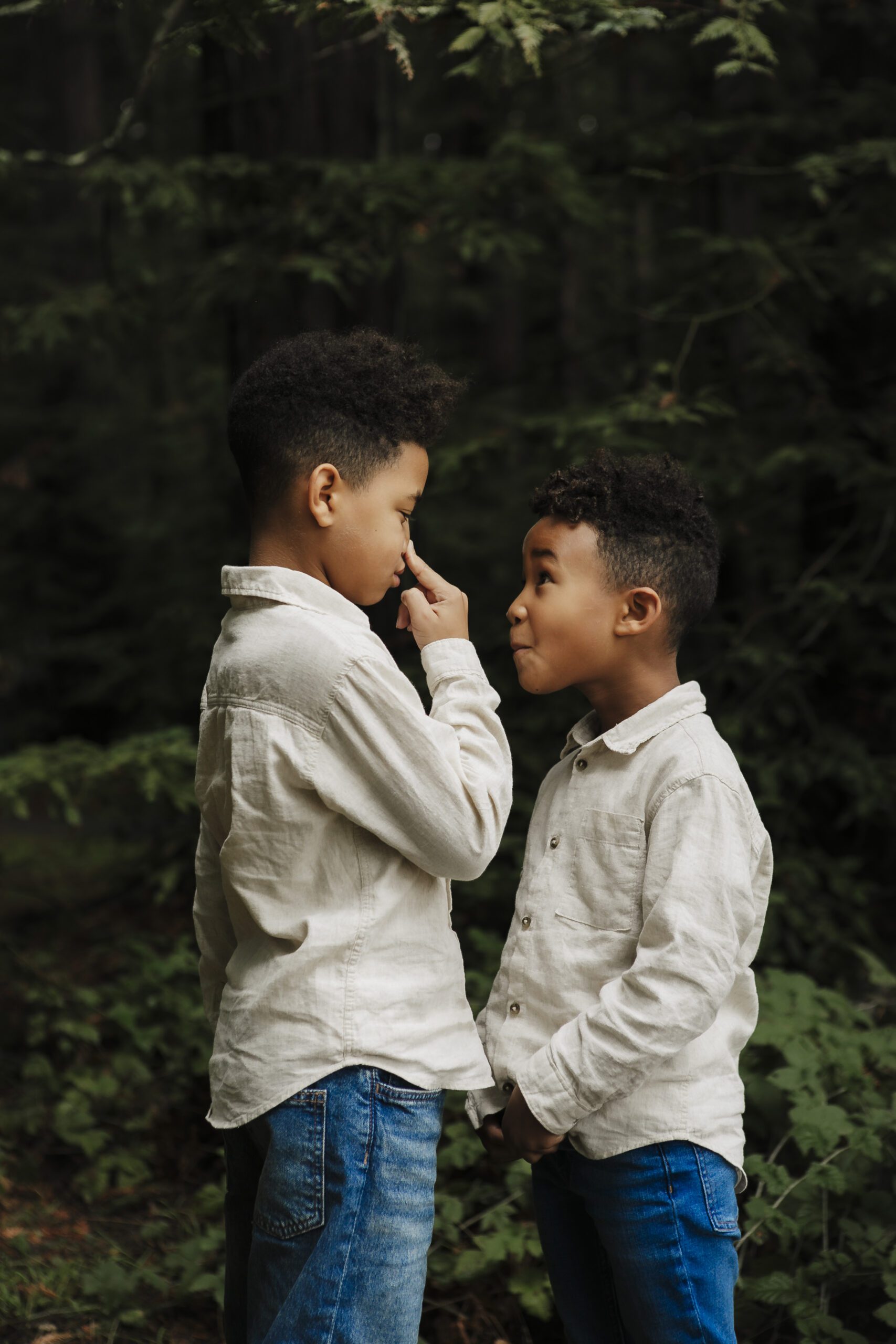 St. Louis family photographer, two young brothers in linen shirts teasing each other among evergreen trees