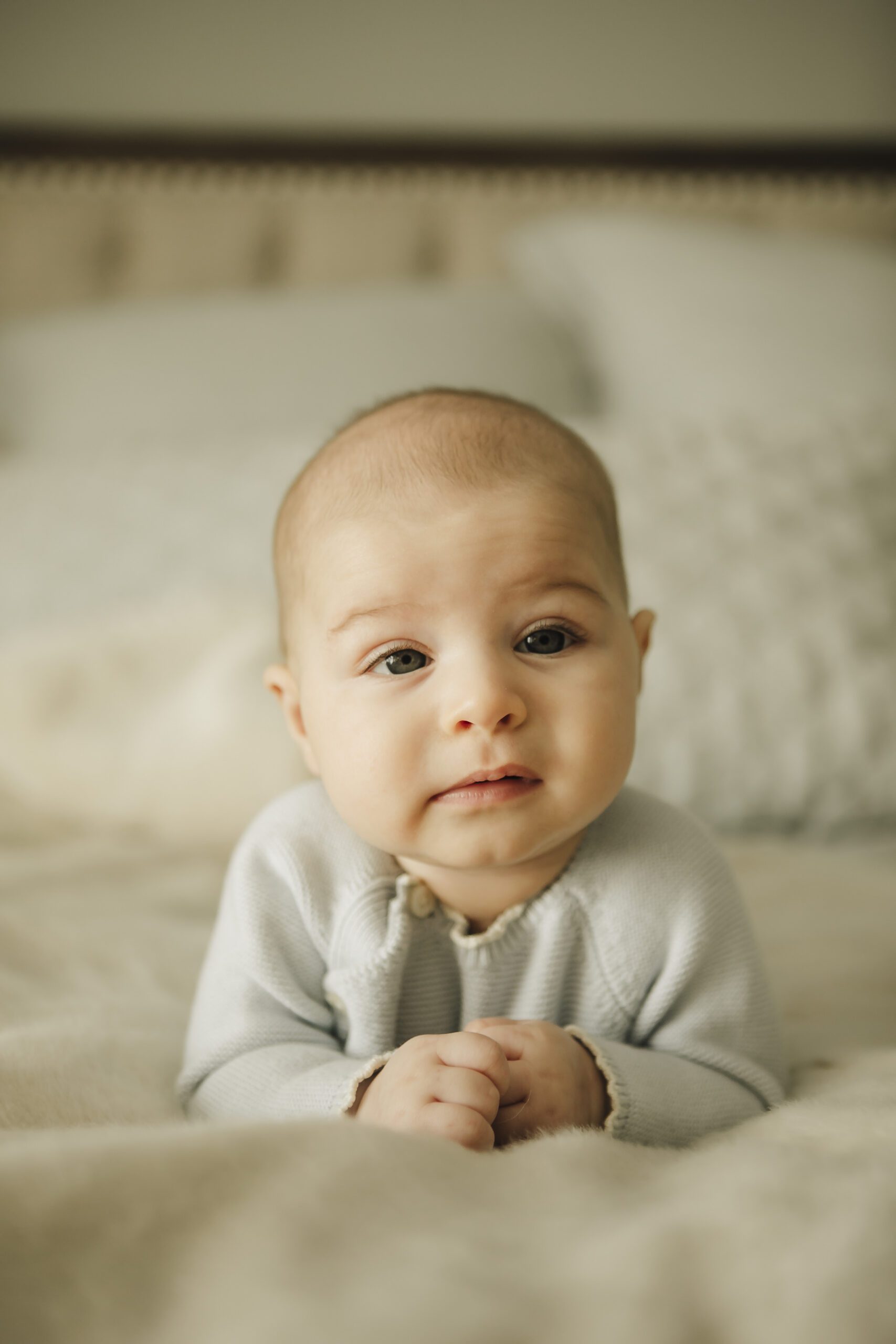 St. Louis newborn photographer, baby boy in a light blue knit sweater doing tummy time on a bed and looking at the camera