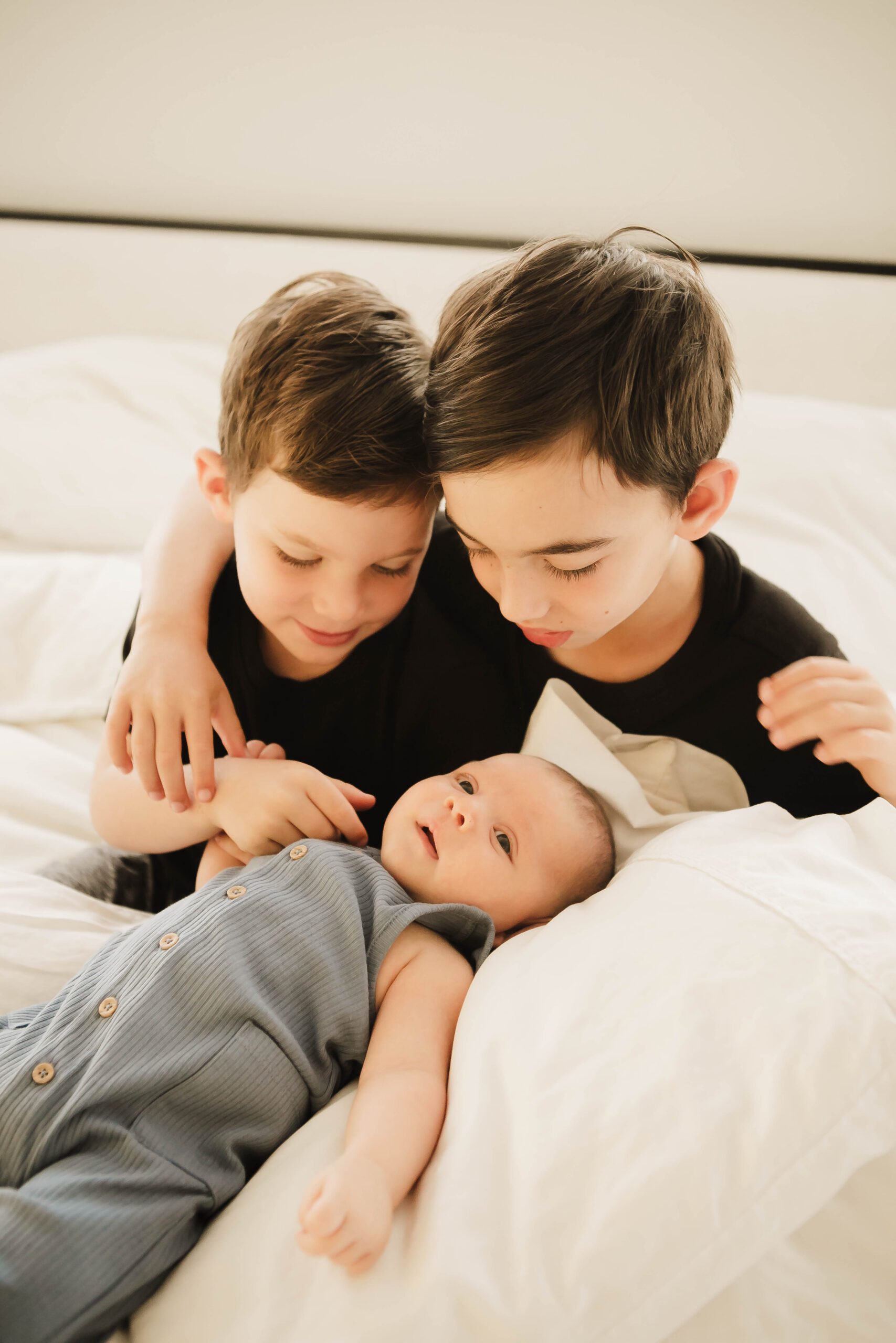 St. Louis newborn photographer, two older brothers leaning over their newborn sibling on a bed
