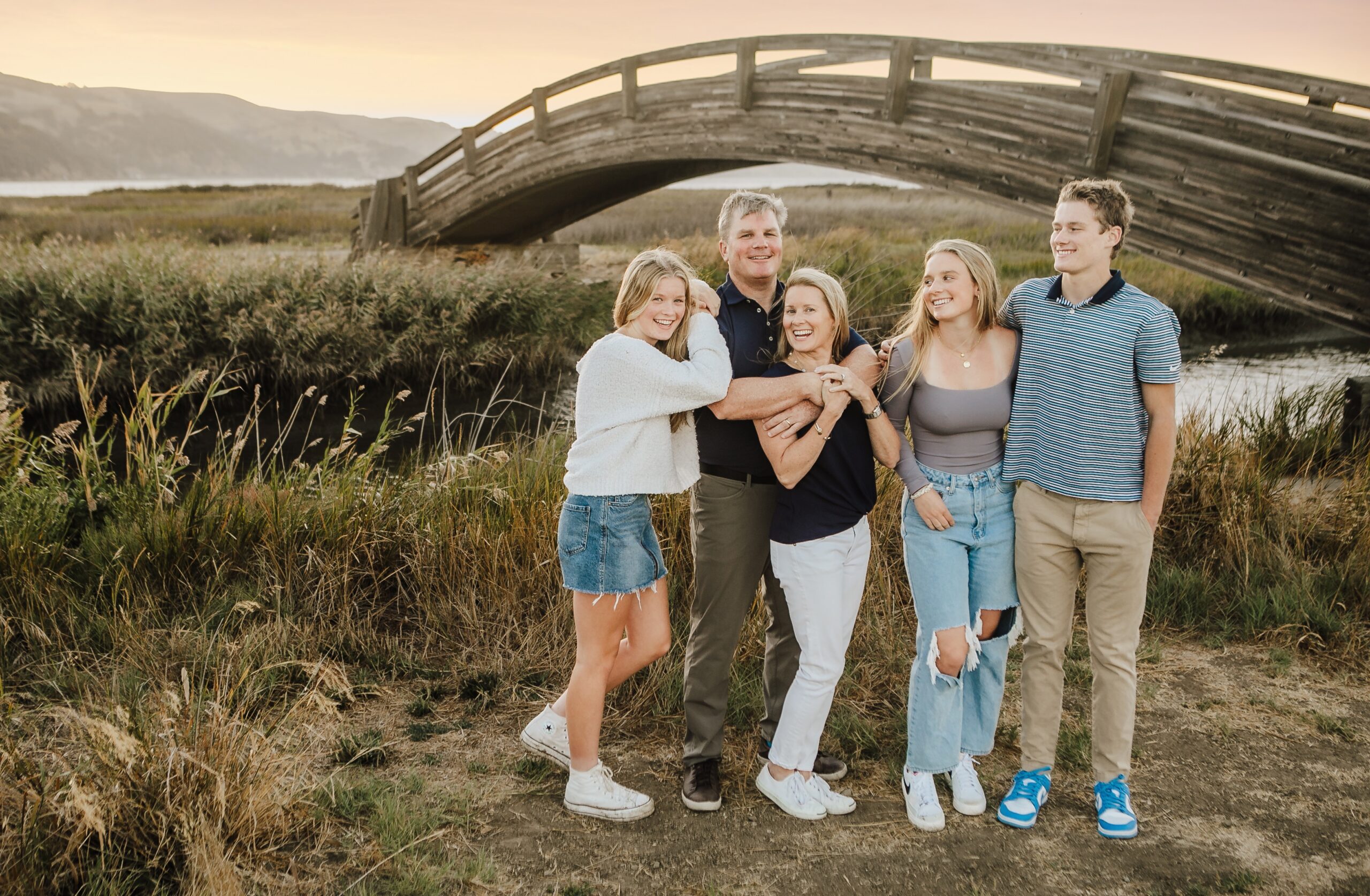 St. Louis family photographer, family of five with their teenagers hugging their parents in front of an arched wooden bridge