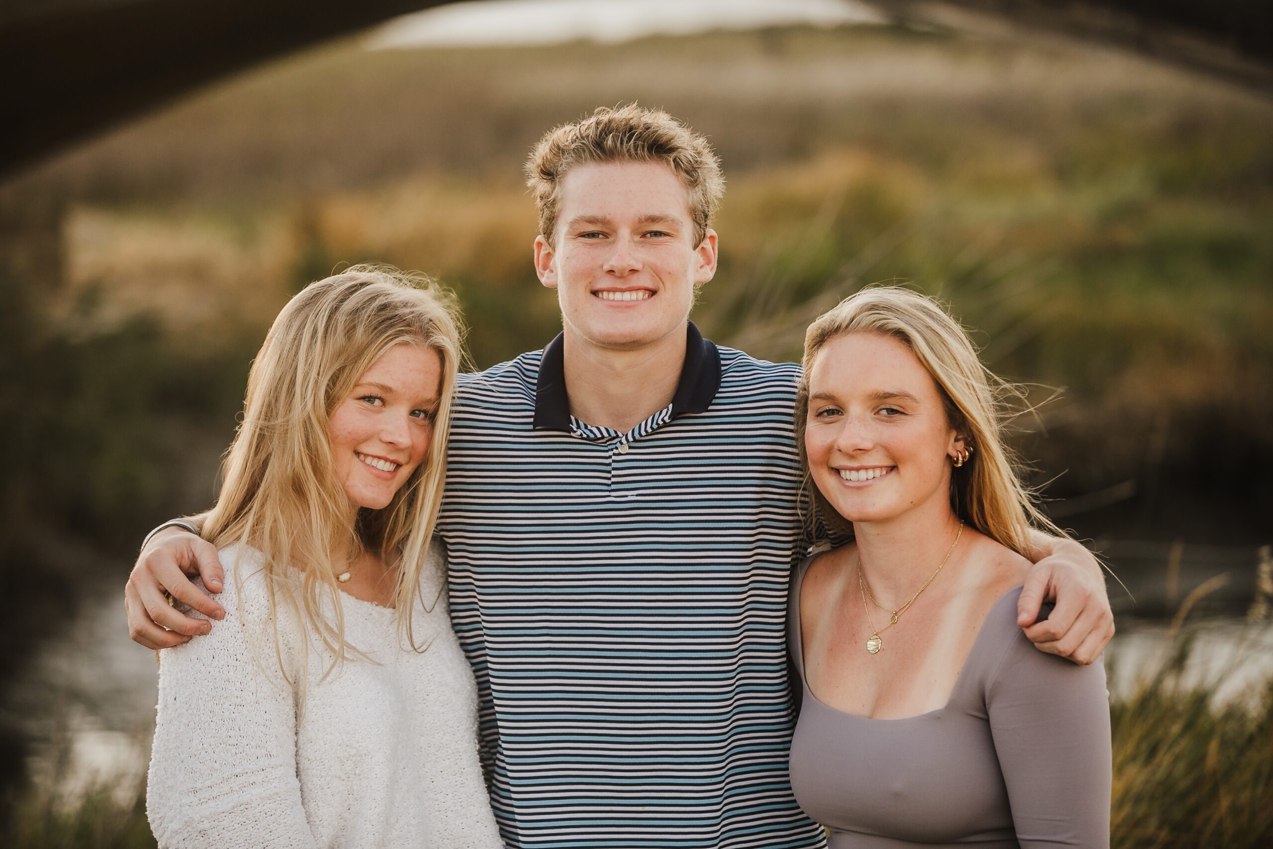 St. Louis family photographer, three teenage siblings standing arm in arm in warm evening light
