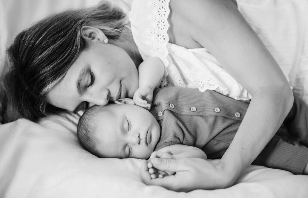 St. Louis newborn photographer, black and white photo of a mother resting her cheek against her sleeping newborn on a soft white bed