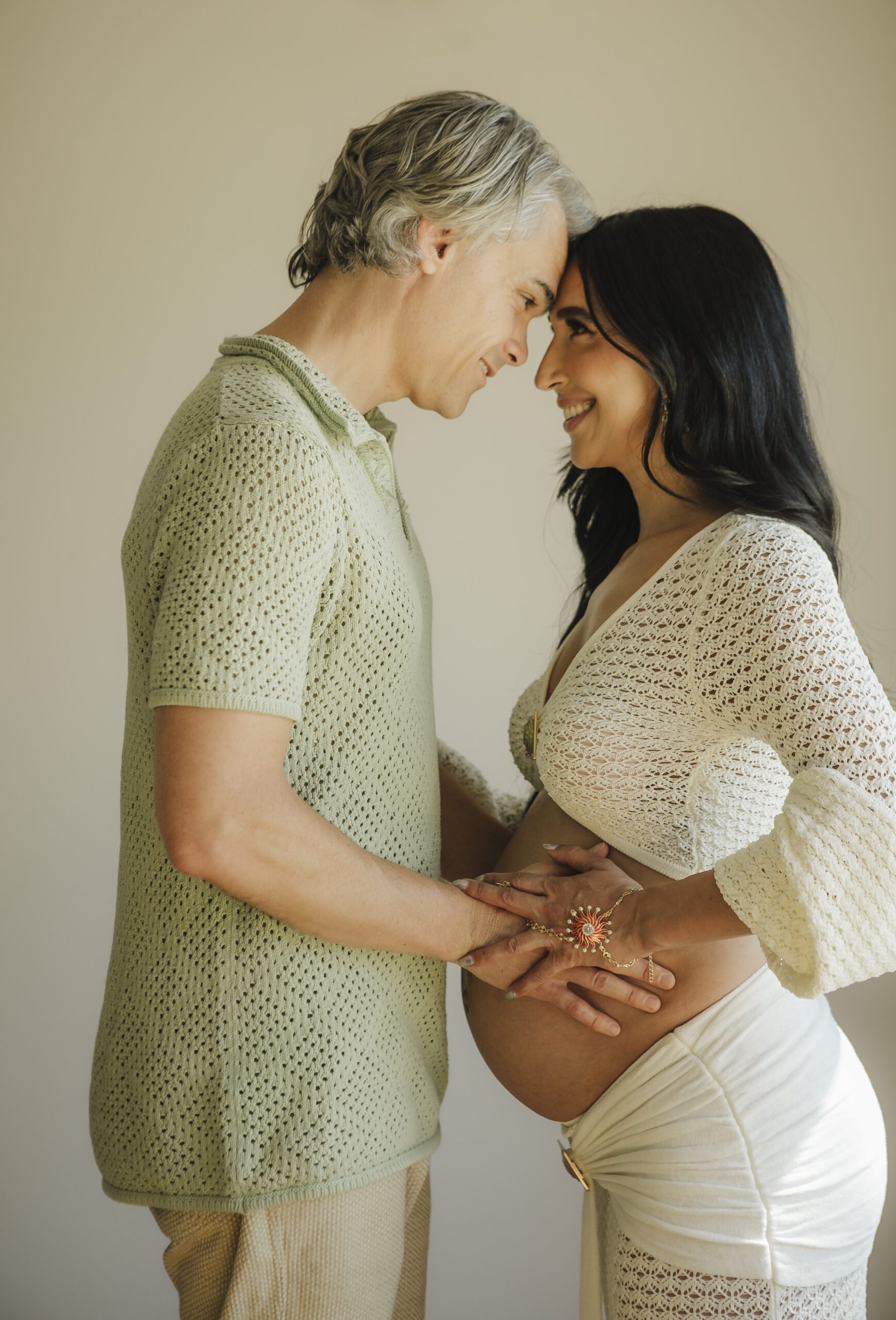 St. Louis maternity photographer, expecting couple with foreheads together and hands resting on the belly in a bright studio