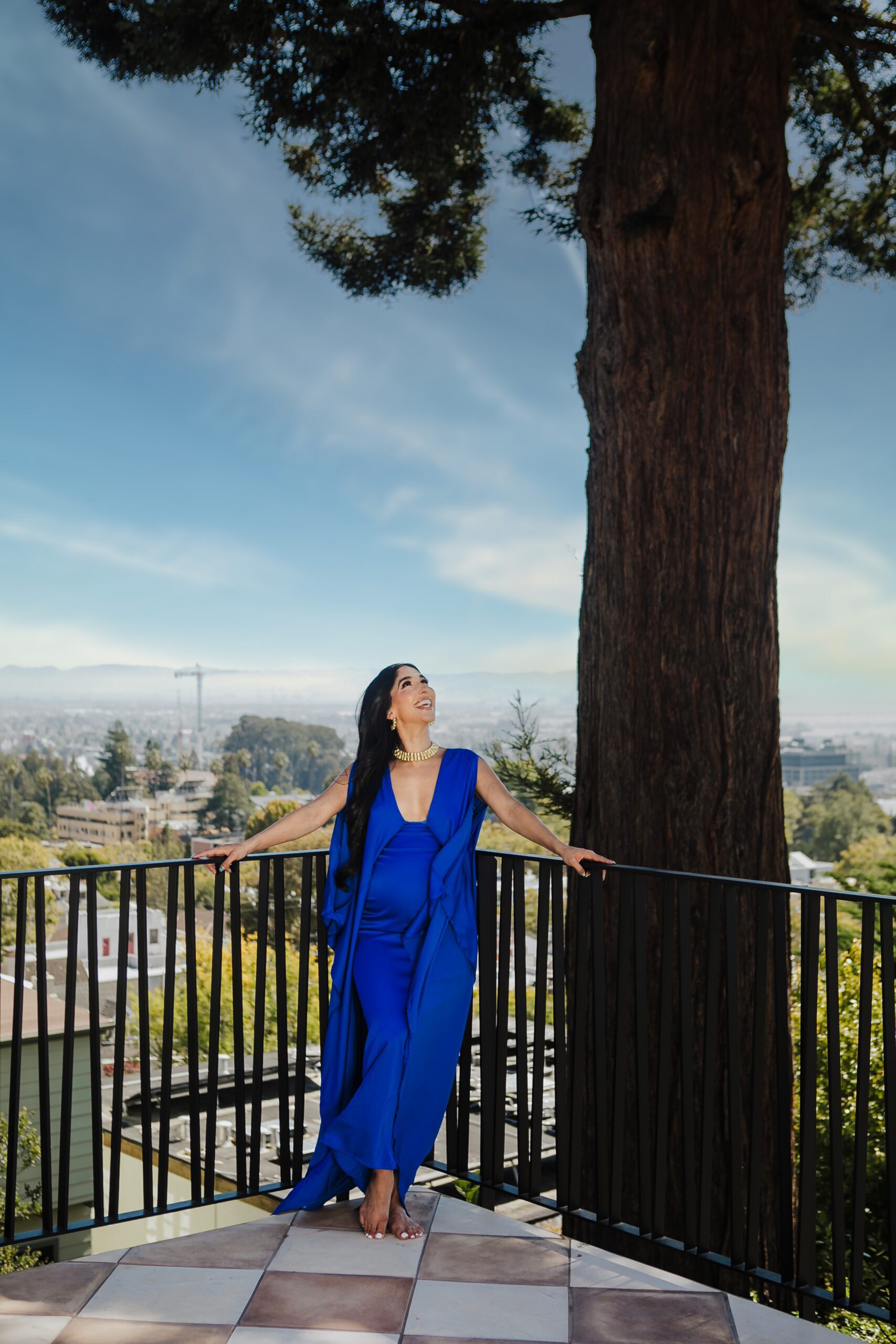 St. Louis maternity photographer, expecting mother in a royal blue gown on a tiled balcony overlooking a hillside and distant valley