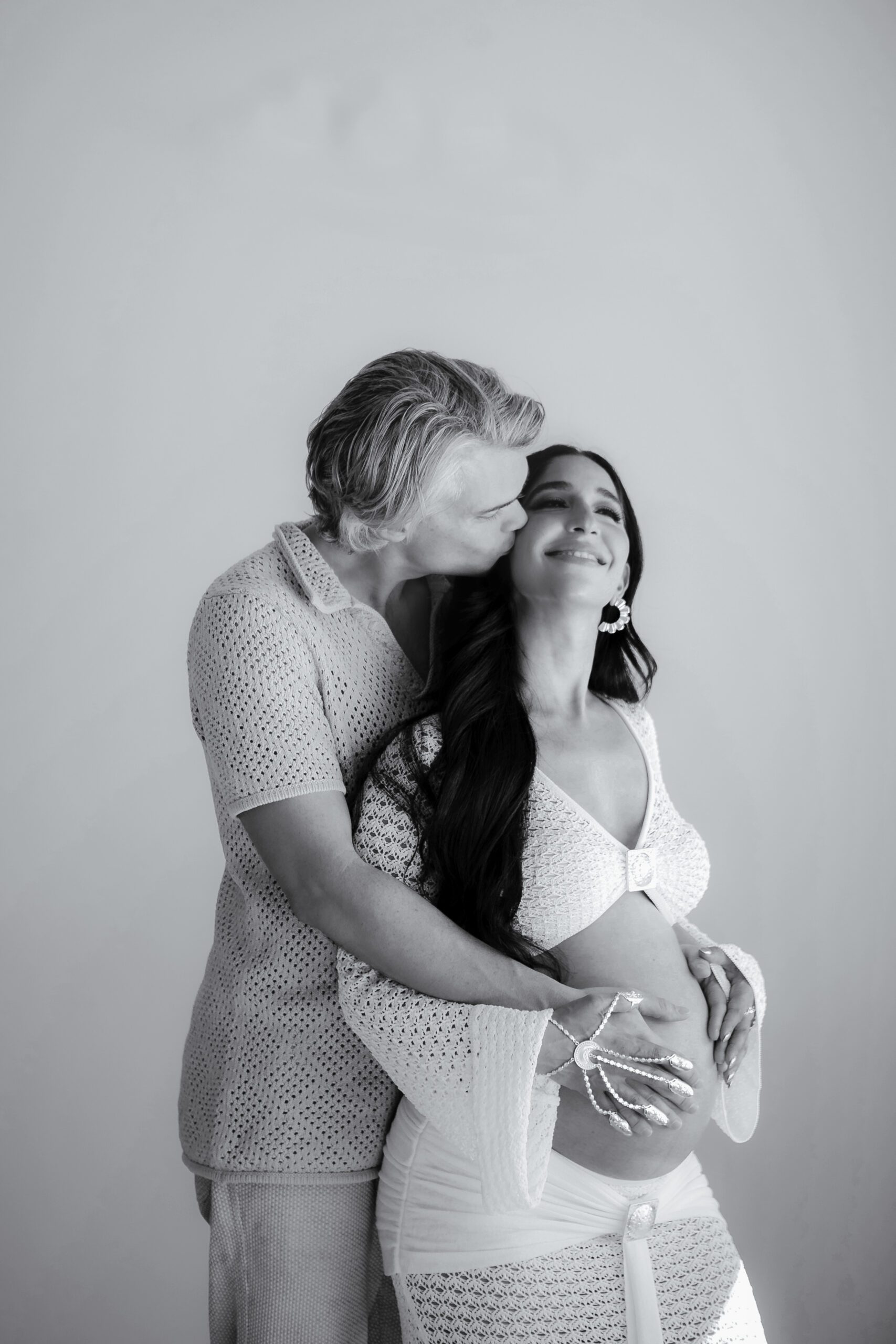 Black and white maternity portrait by a St. Louis maternity photographer, expecting couple embracing with hands on the belly in a bright studio