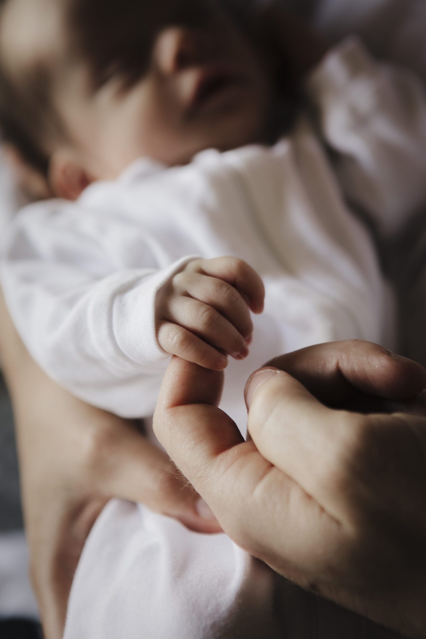 St. Louis newborn photographer, close up of a newborn's tiny hand wrapped around an adult finger, baby sleeping in a white outfit