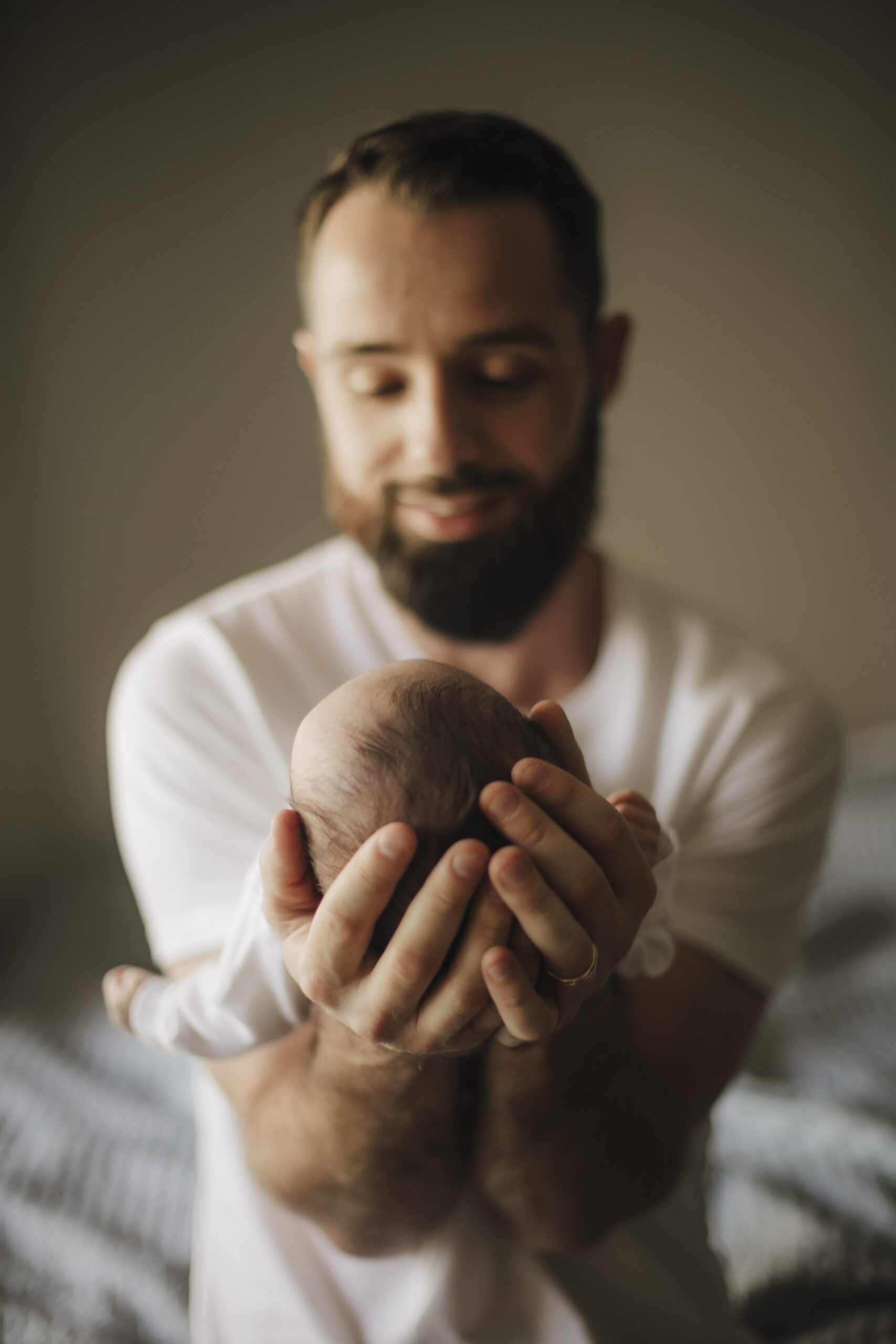 St. Louis newborn photographer, smiling bearded father in a white shirt cradling his sleeping newborn's head in both hands