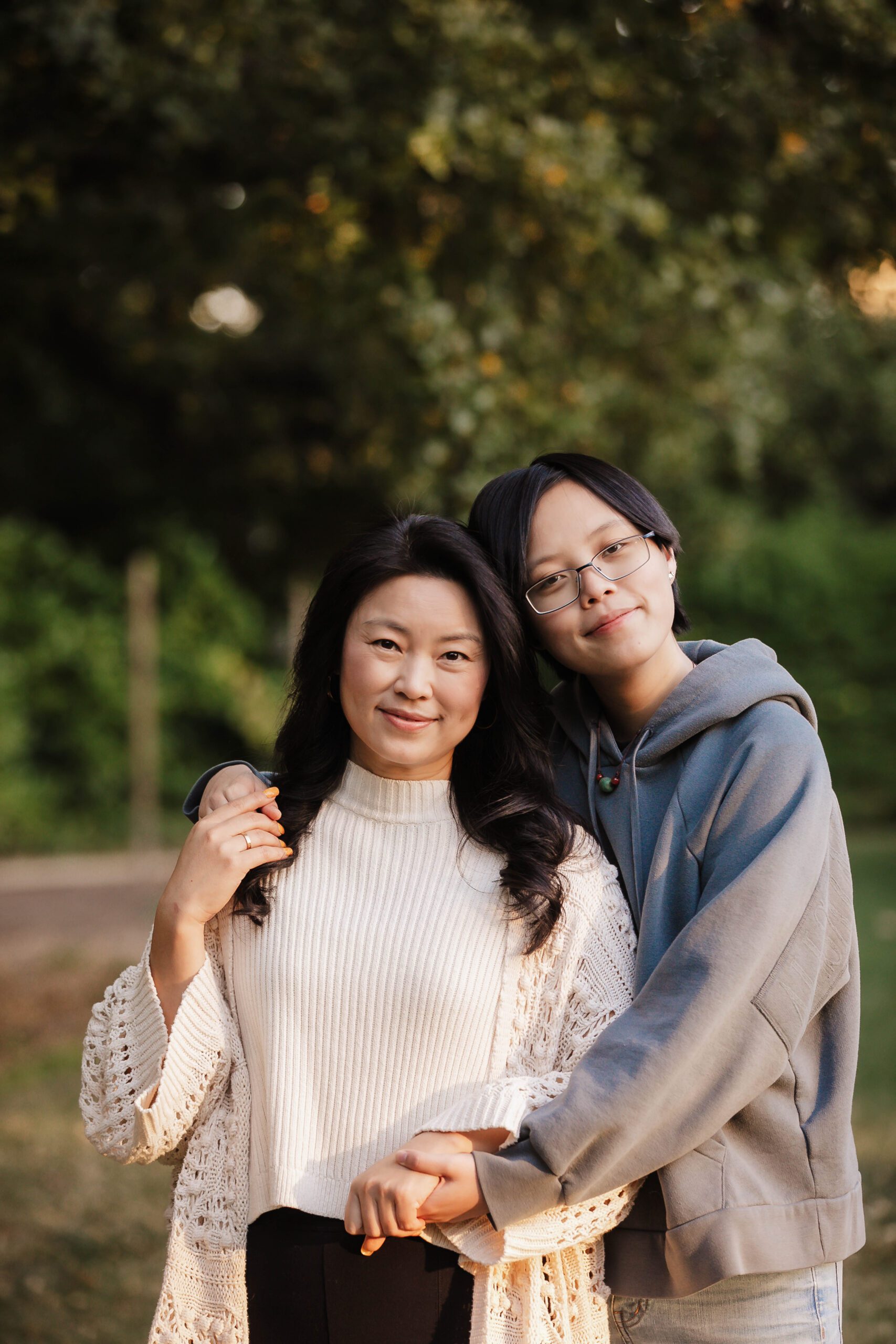 St. Louis family photographer, teenager hugging their mother from behind in a park at sunset